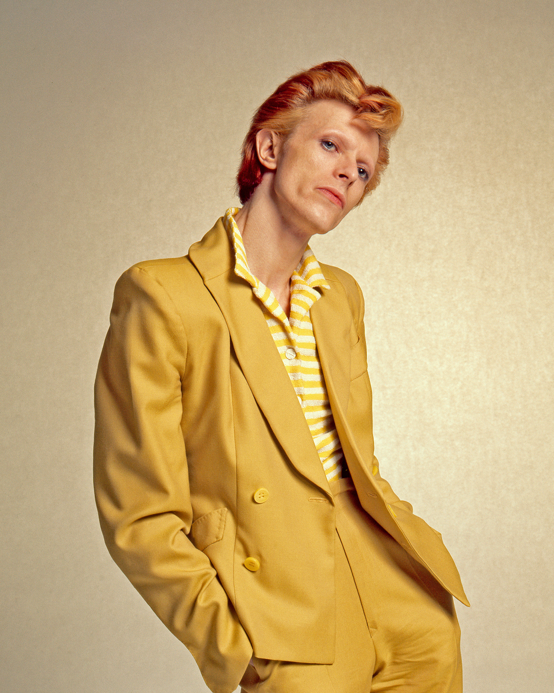 Portrait of a person in a bright yellow suit with a striped shirt, posing against a neutral background.
