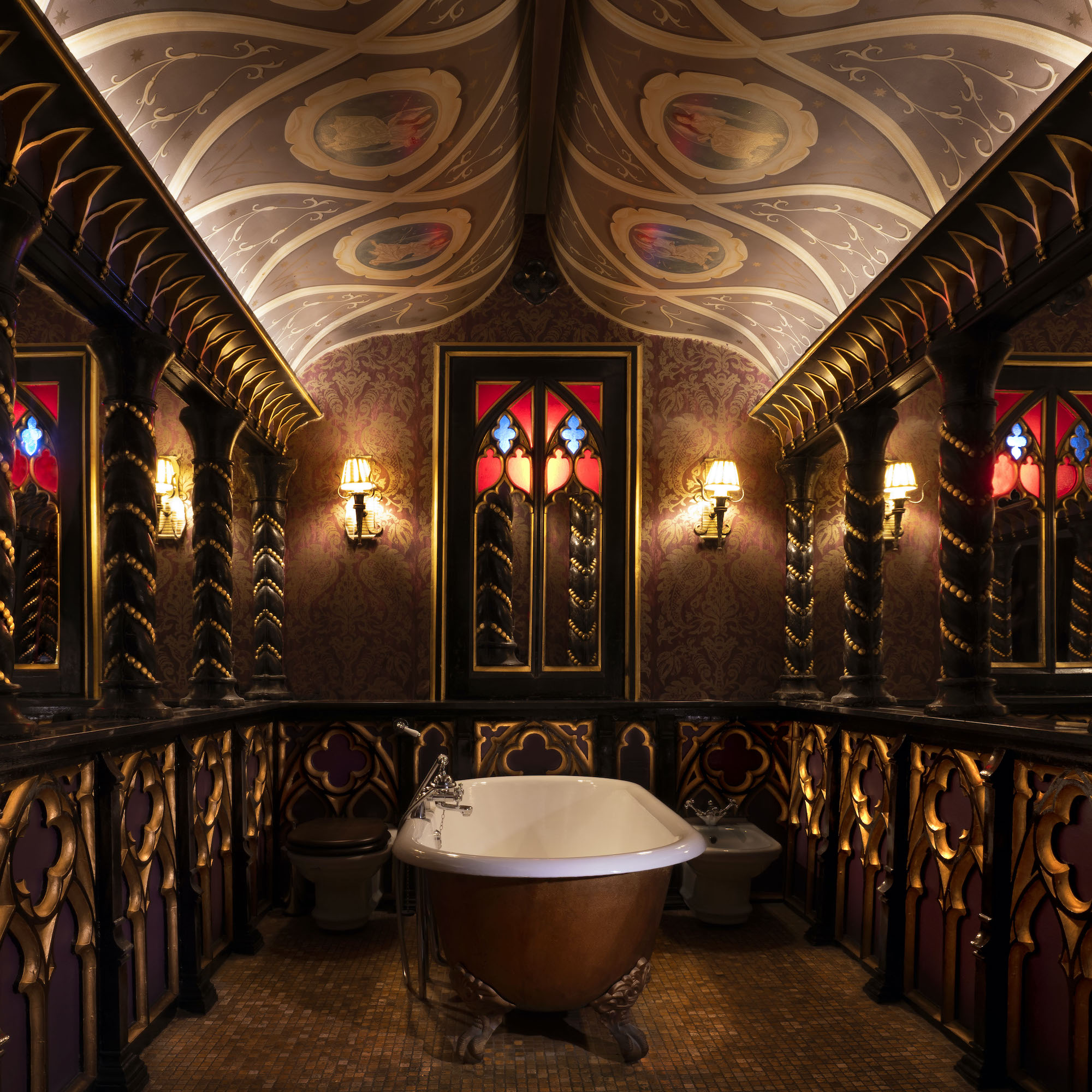 An ornate bathroom featuring a vintage freestanding bathtub, intricately designed walls with purple and gold accents, decorative pillars, and stained glass windows.